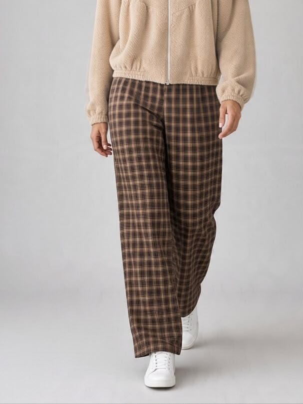Bruine Chastar broek Linette met ruitdessin en lange, rechte pijpen, van voren op een model met een lichte jas.