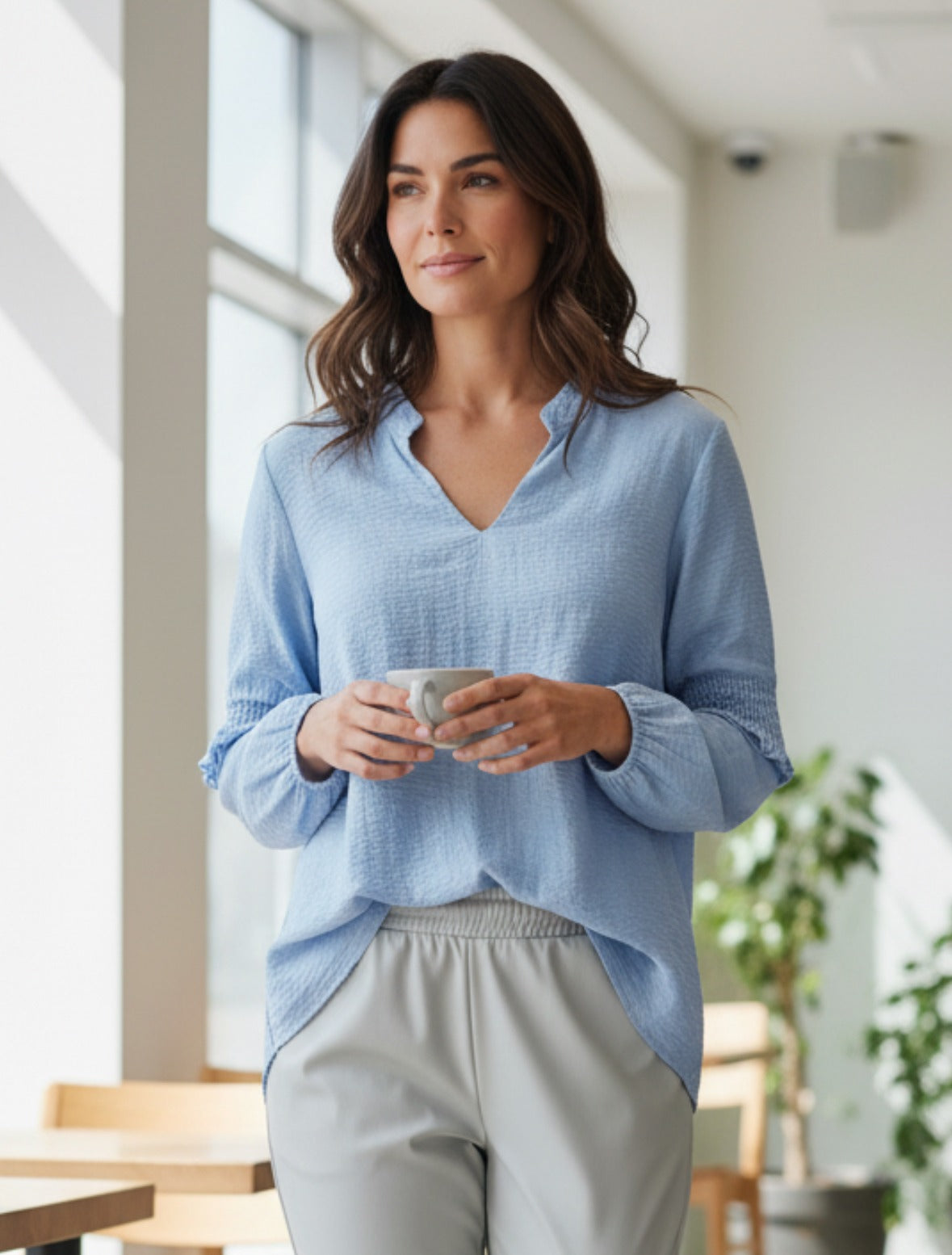 Lichtblauwe viscose blouse met V-hals, structuur in de stof en smokdetails op de lange mouwen, op een model.