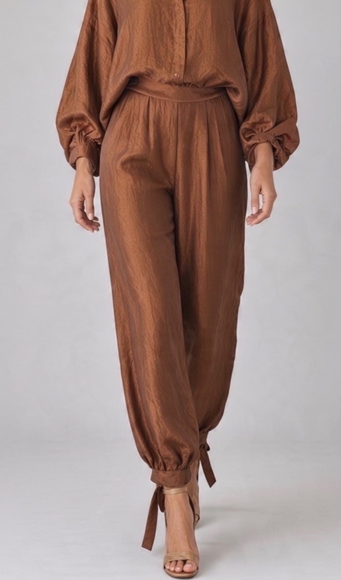 Roestkleurige Chastar broek met plooien en strikken bij de enkels, op een model met een bijpassende blouse.