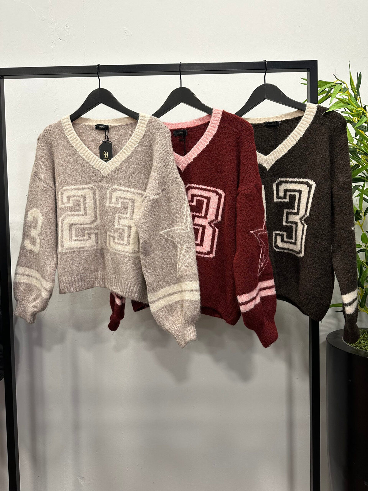 Chastar Trui Soraya in beige, bordeaux en bruin met V-hals, contrastboorden en nummer 23, aan een kledingrek.